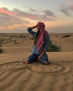 a woman sitting in the middle of a desert with her head scarf around her neck