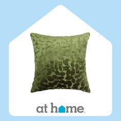 a green pillow sitting on top of a blue and white background with the at home logo below it