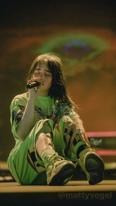 a woman with long hair sitting on the ground while holding a microphone in her hand