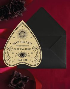 save the date card with an all seeing eye on it next to red roses and black envelope