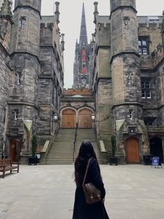 a woman standing in front of an old castle like building with stairs leading up to it