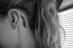 a woman's ear with a small feather tattoo on it