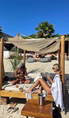 two women are sitting on the beach under a canopy