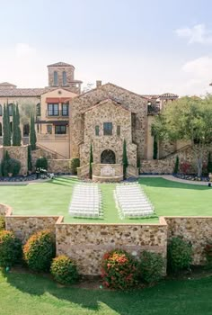 an outdoor ceremony set up in front of a large building with stone walls and white chairs