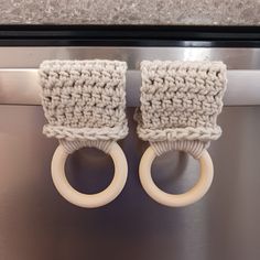 two crocheted wooden rings are hanging from the handle of a stainless steel dishwasher