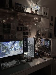 two computer monitors sitting on top of a desk in front of a wall with pictures