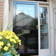 a black front door with yellow flowers and a house number sign on it's side