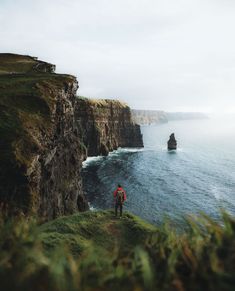 a man standing on the edge of a cliff overlooking the ocean with cliffs in the background