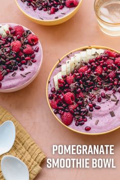 two bowls filled with smoothie topped with raspberries and bananas next to spoons