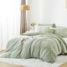 a bed with green comforters and pillows on top of a white rug next to a window