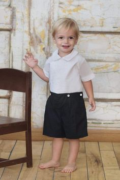 a little boy standing next to a chair in front of a white wall and wooden floor