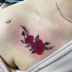 a woman's chest with red roses and leaves tattooed on her left side shoulder