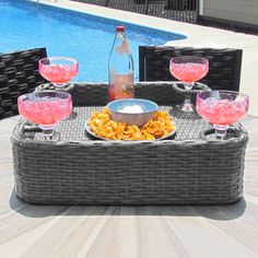 a wicker tray with wine glasses and food on it next to a swimming pool