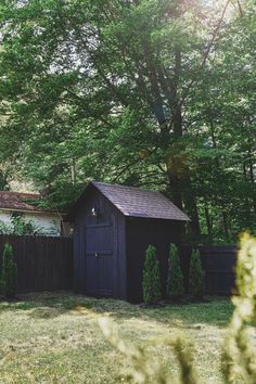 an outhouse in the middle of a yard surrounded by trees and bushes with sun shining on it