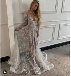 a woman standing in front of a white wall wearing a long dress with sequins