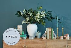 a vase with flowers and candles sitting on a dresser next to a sign that says vintage new york