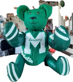 a green teddy bear with the letter m on it's chest and arms outstretched