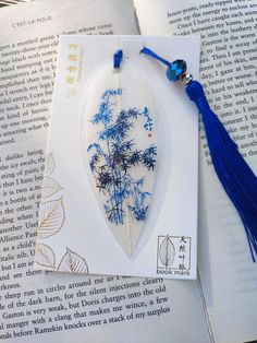 a blue tasseled bookmark on top of an open book with a tree in it