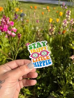 someone holding up a sticker that says stay happy little hippie in front of some flowers