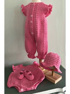 a pink knitted baby outfit and hat on a wooden stand next to a white wall