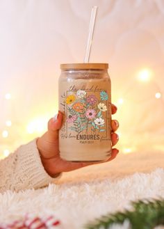 a person holding a mason jar with flowers on it and a straw in the top