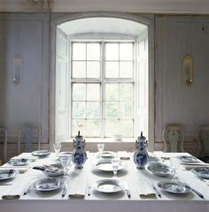 an empty table with plates and silverware on it in front of a large window