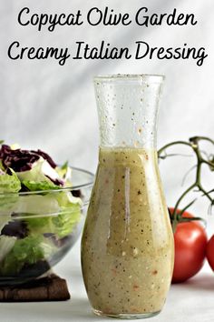 a salad dressing in a glass bottle next to a bowl of salad greens and tomatoes