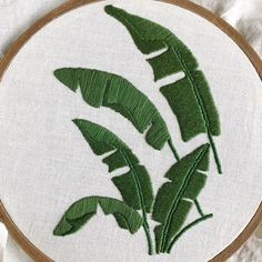 a close up of a embroidery on a piece of cloth with some green leaves in it