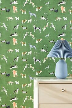 a blue lamp sitting on top of a dresser next to a green wallpaper covered in dogs