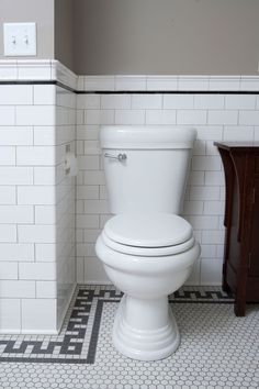 a white toilet sitting in a bathroom next to a wooden cabinet and tiled flooring