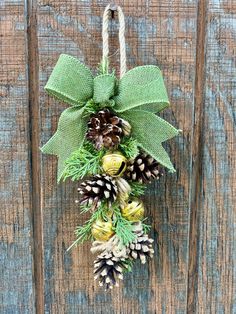 a wreath with pine cones and evergreens hanging on a wooden door hanger that is tied to a rope