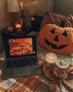 a laptop computer sitting on top of a bed next to a cup of coffee and a pumpkin pillow