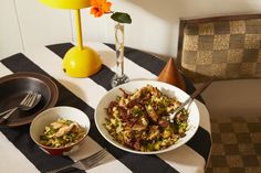 a table topped with two bowls of food and a vase filled with flowers on top of it