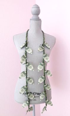 a gray mannequin with green leaves on it's neck and two rows of beads