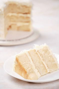 a slice of white cake on a plate next to the rest of the cake in the background