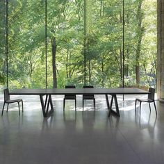 a table and chairs in front of large windows with trees outside the glass wall behind them