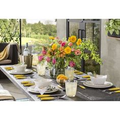 a dining table set with plates, cups and vases filled with flowers on it