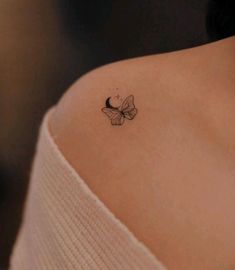 a small butterfly tattoo on the back of a woman's left shoulder, which is black and white