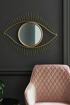 an eye shaped mirror hangs on the wall next to a pink chair and side table