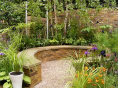 a stone bench in the middle of a garden with flowers and plants growing around it