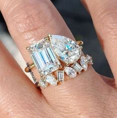 a woman's engagement ring with an emerald and diamond center stone on her finger