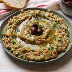 a plate filled with hummus and olives on top of a table next to bread