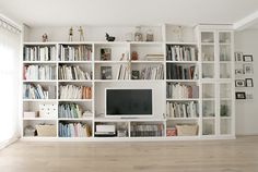 a living room filled with lots of white bookshelves and a flat screen tv