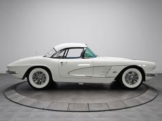 an old white car sitting on top of a circular display case in a room with gray walls