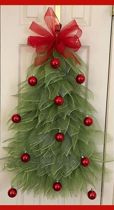 a christmas tree made out of green leaves and red baubles hanging on a door