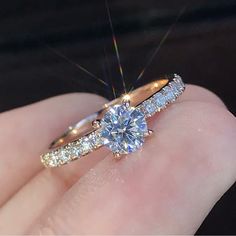 a woman's hand holding a diamond ring on top of her finger, with the engagement band set in yellow gold