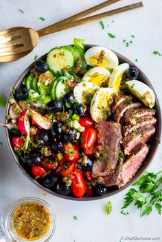 a bowl filled with meat and vegetables next to a fork, spoon and small dish