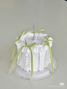 a white cake with green ribbon and an apple on top