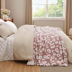 a bed with a pink and white comforter on top of it next to a window