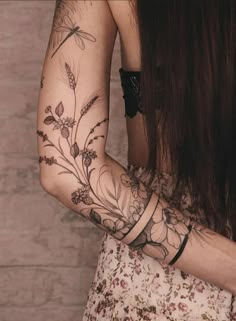 a woman's arm with flowers and dragonflies tattooed on her left arm, next to a brick wall